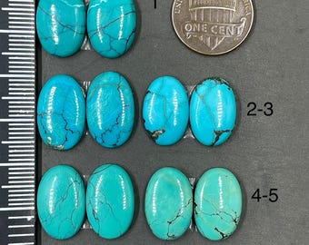 May include: Eight oval turquoise cabochons with dark matrix veining arranged in three rows next to a ruler and a US one cent coin. The stones are bright blue with varying patterns of black lines. The text TA654 is printed at the bottom right.