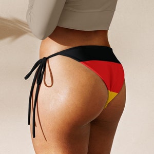 Könnte beinhalten: Eine Frau trägt ein hellgraues, langärmliges Crop-Top und einen schwarzen und roten Bikini-Höschen mit einem gelben Streifen. Das Bikini-Höschen hat einen seitlichen Knoten.