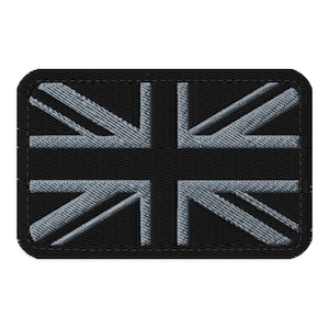 Op de afbeelding: Een rechthoekige zwarte patch met de Union Jack, de vlag van het Verenigd Koninkrijk. Het vlagontwerp is uitgevoerd in grijstinten, met een gedetailleerde geborduurde textuur. De patch heeft een gestikte rand.