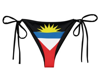Puede incluir: Braga de bikini negra con un diseño de nudo lateral que presenta la bandera de Antigua y Barbuda. La bandera es roja, blanca, azul y amarilla con un sol en el centro.