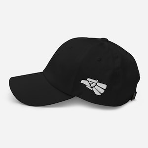 May include: Black baseball cap with a white embroidered eagle design on the side. The cap has a curved brim and an adjustable strap at the back. A classic, casual accessory.