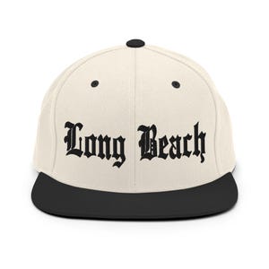 Könnte beinhalten: Eine beige und schwarze Baseballkappe mit dem Schriftzug "Long Beach" in schwarzer Stickerei auf der Vorderseite.