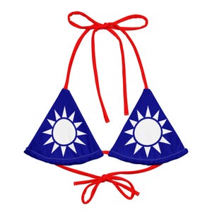 May include: A red and blue bikini top with a triangle shape. The top features a sun with 12 rays on a blue background. The sun is white with a blue outline.