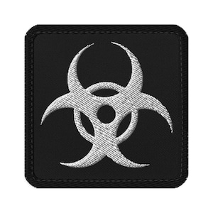 Pode incluir: Um patch quadrado preto com um símbolo de perigo biológico branco bordado. O símbolo é uma representação estilizada de um aviso de perigo, com três braços curvos irradiando de um círculo central. O patch tem uma borda costurada.