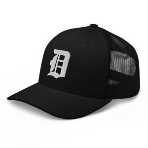 Könnte beinhalten: Schwarze Trucker-Kappe mit einem weißen gestickten Buchstaben D auf der Vorderseite. Die Kappe hat ein Netzrücken.