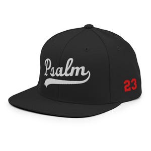 Op de afbeelding: Zwarte baseballpet met een platte klep. Het woord "Psalm" is in witte letters op de voorkant geborduurd. Het nummer "23" is rood op de zijkant geborduurd. Een klassiek, stijlvol accessoire.