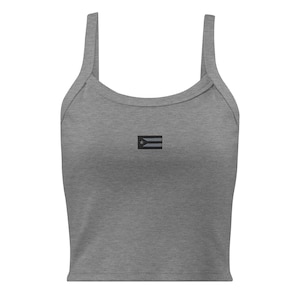 May include: A gray tank top with a scoop neck and thin straps. The top features a small black and white flag emblem on the front, centered below the neckline. The fabric appears to be a soft, knit material.