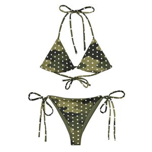 May include: A two-piece bikini set featuring a camouflage pattern with white polka dots. The top is a halter style with tie closures, and the bottoms are a classic tie-side design. The color palette includes shades of green, brown, and white.