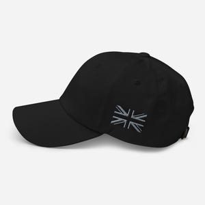 Peut inclure: Casquette de baseball noire avec une visière incurvée. La casquette présente un drapeau Union Jack gris clair brodé sur le côté. La casquette est en matière souple et possède une sangle réglable.