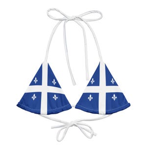 May include: A blue and white bikini top featuring the flag of Quebec. The top has a triangle shape with white straps and ties. The design includes a white cross and fleur-de-lis symbols on a blue background.