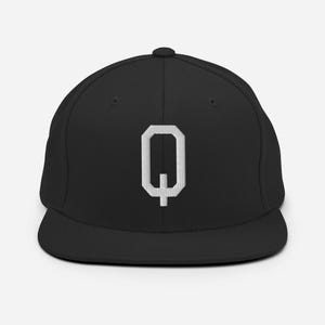 May include: A black baseball cap with a white, stylized letter "Q" embroidered on the front. The cap has a flat brim and a rounded crown, with a small button on top.