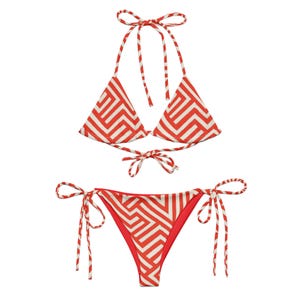 Könnte beinhalten: Ein zweiteiliger Bikini mit einem rot-weißen geometrischen Muster. Das Oberteil ist im Neckholder-Stil mit Dreiecks-Cups und einem Kordelverschluss. Die Hose ist im String-Stil mit Bindebändern an den Seiten. Der Bikini ist aus leichtem Stoff gefertigt.