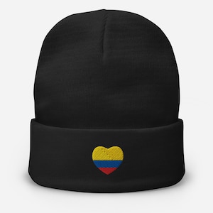Pode incluir: Gorro preto com um emblema em forma de coração com as cores da bandeira colombiana: amarelo, azul e vermelho. O gorro é feito de um material de malha macia e tem uma bainha dobrada.