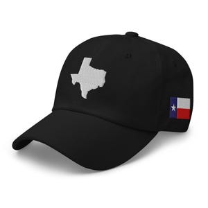 May include: Black baseball cap featuring a white embroidered outline of the state of Texas on the front. The Texas flag is embroidered on the side. The cap has a curved brim and an adjustable strap.