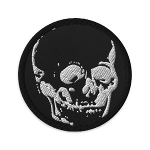 Könnte beinhalten: Runder, schwarzer, gestickter Aufnäher mit einem weißen Totenkopf-Design. Der Totenkopf zeigt Zähne, Augenhöhlen und Nasenhöhle. Der Aufnäher hat einen schwarzen Rand. Geeignet für Jacken, Taschen oder andere Kleidungsstücke.