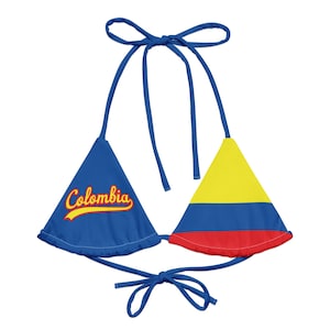 May include: A blue bikini top with the word "Colombia" in yellow script on one cup. The other cup features the yellow, blue, and red colours of the Colombian flag. The top has blue ties.