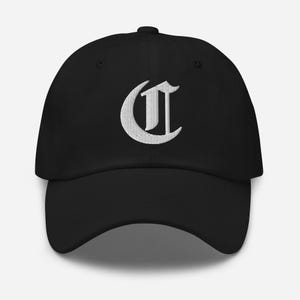 Könnte beinhalten: Schwarze Baseballkappe mit einem weißen, gestickten gotischen Buchstaben "C" auf der Vorderseite. Die Kappe hat einen gebogenen Schirm und einen verstellbaren Riemen am Hinterkopf. Der Hut ist aus weichem, strapazierfähigem Stoff.