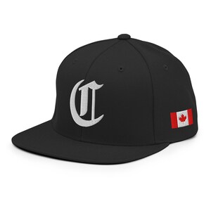 May include: Black baseball cap with a flat peak. The cap has a white, ornate letter "C" embroidered on the front and a Canadian flag patch on the side. The hat is made of a sturdy material and has a structured fit.
