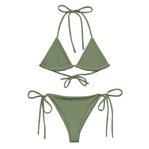 Peut inclure: Ensemble de bikini vert olive. Le haut est de style triangle avec des liens à nouer autour du cou et du dos. Le bas est de coupe classique avec des liens sur les côtés. Le tissu est lisse.