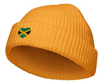 May include: Mustard yellow knit beanie with a folded brim. A heart-shaped patch featuring the Jamaican flag is embroidered on the front. The hat is made of a ribbed knit material.