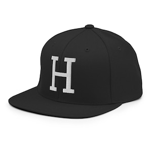 May include: A black baseball cap with a flat brim. The cap features a white embroidered letter "H" on the front. The hat is a classic style, suitable for casual wear.