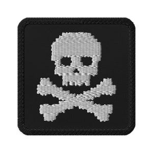 Może przedstawiać: Haftowana naszywka z białym motywem czaszki i skrzyżowanych piszczeli na czarnym kwadratowym tle. Czaszka ma kwadratowe oczodoły i zęby. Naszywka ma czarną obwódkę.