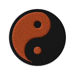 Puede incluir: Un símbolo yin yang negro y naranja bordado en un parche circular.