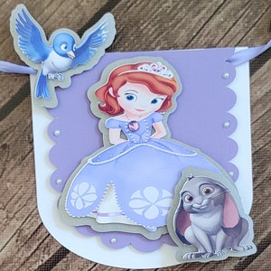 May include: A purple banner with a princess character, a blue bird, and a gray rabbit. The princess is wearing a purple dress with white flowers and a crown. The banner has a scalloped edge with white pearls.