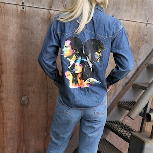 May include: A denim shirt and jeans outfit. The blue denim shirt has a colourful graphic on the back. The jeans are light wash denim. The outfit is worn with trainers.