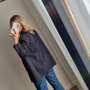 May include: A black blazer with long sleeves and a relaxed fit. The blazer is worn over a white shirt and blue jeans.