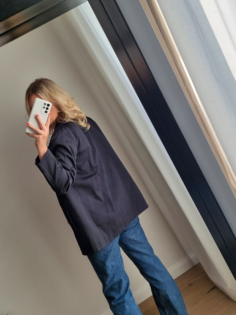May include: A black blazer with long sleeves and a relaxed fit. The blazer is worn over a white shirt and blue jeans.