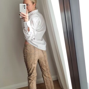 May include: A white button-down shirt and brown patterned pants are reflected in a mirror. The pants have a subtle textured design. The outfit is paired with black shoes. The image is taken indoors.