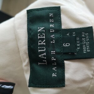 May include: A white label with green trim and the text "RALPH LAUREN" in white. The label also has a smaller white label with the text "6" and "MADE IN U.S.A." in black. The label reads "FABRIQUE AU ETATS-UNIS".