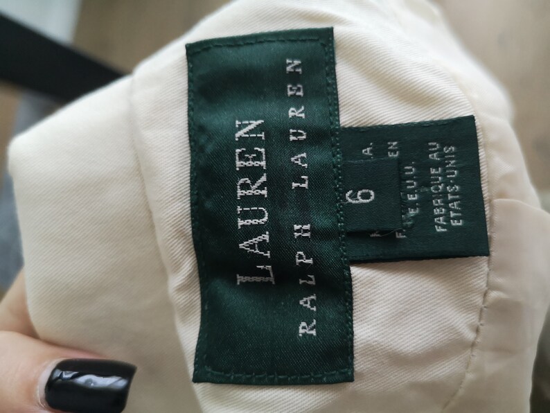 May include: A white label with green trim and the text "RALPH LAUREN" in white. The label also has a smaller white label with the text "6" and "MADE IN U.S.A." in black. The label reads "FABRIQUE AU ETATS-UNIS".