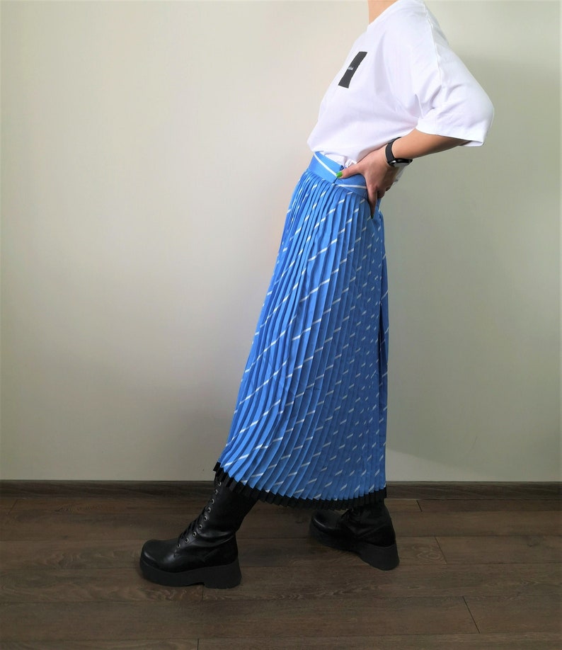 May include: A blue pleated skirt with a white stripe pattern. The skirt has a black lace trim and is paired with black boots.