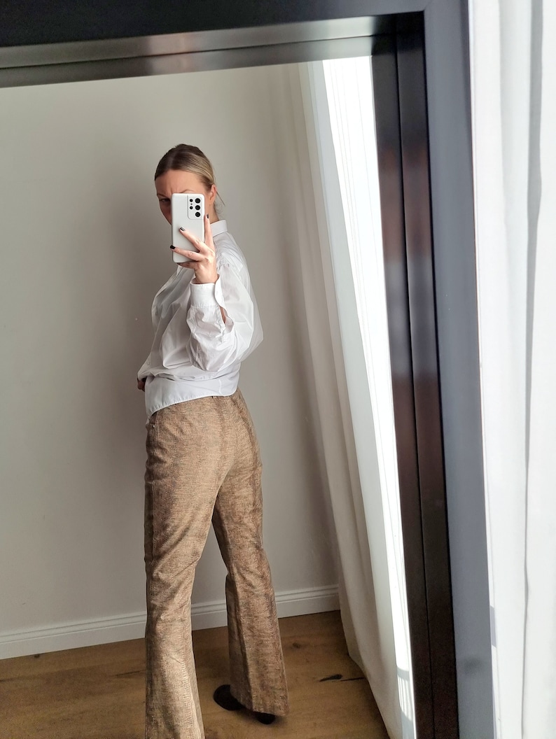 May include: A white button-down shirt with rolled-up sleeves and brown flared pants. The pants have a textured, woven appearance. The outfit is reflected in a mirror.
