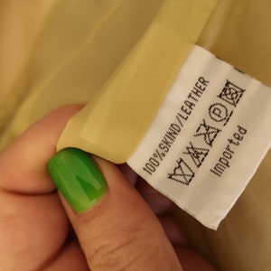 May include: A white tag with black text that reads "100% SKIND/LEATHER" and includes a care label with symbols. The tag also says "Imported".