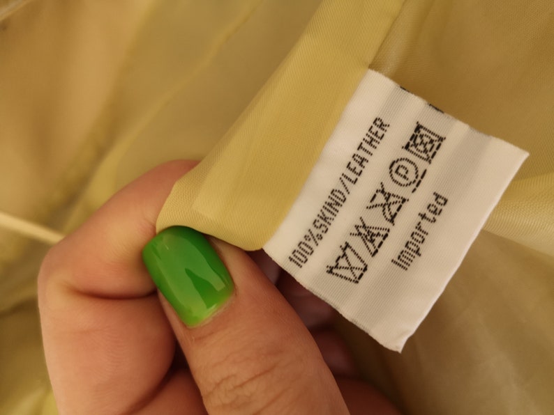 May include: A white tag with black text that reads "100% SKIND/LEATHER" and includes a care label with symbols. The tag also says "Imported".