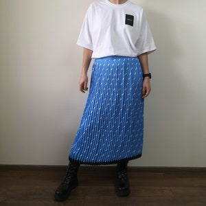 May include: A blue pleated skirt with a white geometric pattern. The skirt has a black waistband and a black trim at the hem.