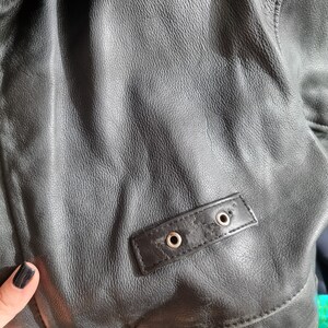 Op de afbeelding: Zwart leren jack met een bontkraag en een klein leren patch met twee metalen oogjes.