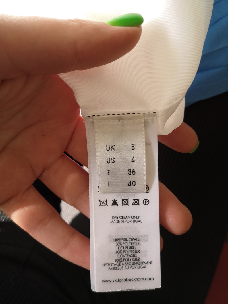 May include: White clothing label with black text and symbols. The label shows size information in UK, US, F, and I sizes. The label also includes care instructions, fabric content, and the brand name "Victoria Beckham".