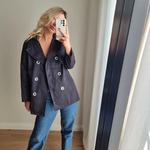 May include: A navy blue double-breasted peacoat with silver button accents. The coat has a collar that can be worn up or down.