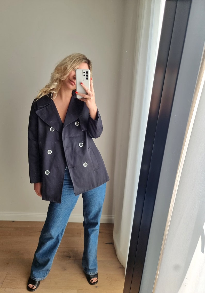 May include: A navy blue double-breasted peacoat with silver button accents. The coat has a collar that can be worn up or down.