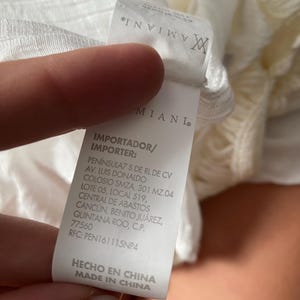 May include: White clothing tag with black text. The text reads "IMPORTADOR/IMPORTER: PEN&Iacute;NSULAZ S DE RL DE CV AV. LUIS DONALDO COLOSIO SMZA. 301 MZ.04 LOTE 05, LOCAL 519, CENTRAL DE ABASTOS CANC&Uacute;N, BENITO JU&Aacute;REZ, QUINTANA ROO, C.P. 77560 RFC: PEN161115NP4 HECHO EN CHINA MADE IN CHINA"