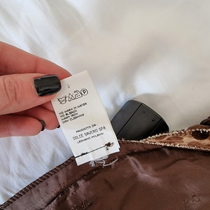 Puede incluir: Una etiqueta de cuidado blanca con texto negro y s&iacute;mbolos. La etiqueta dice "NO WASH IN WATER, NO BLEACH, WARM IRON, DRY CLEANING". Tambi&eacute;n dice "PRODOTTO DA: DOLCE SAVERIO SPA LEGNANO IMILANO".