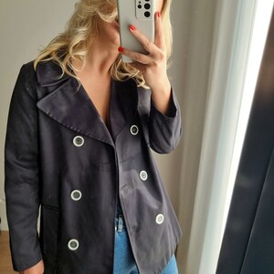 May include: A black double-breasted jacket with white buttons. The jacket is made of a smooth, slightly shiny fabric.