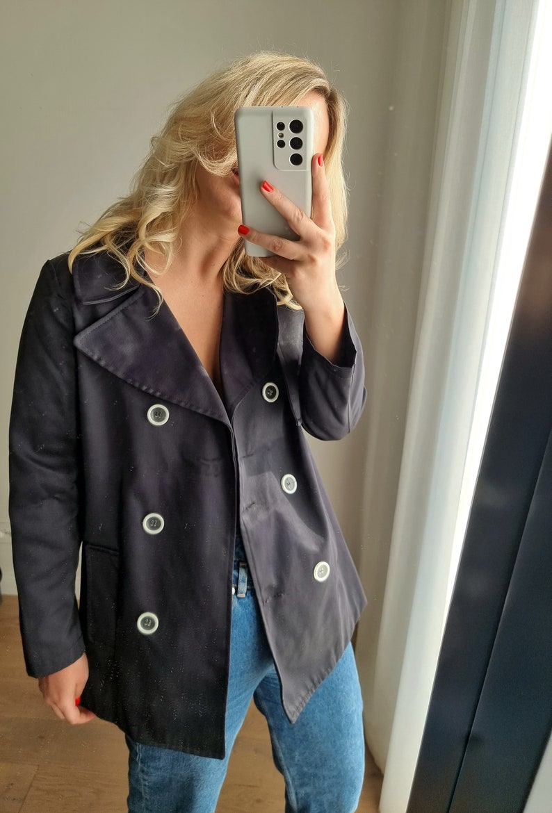 May include: A black double-breasted jacket with white buttons. The jacket is made of a smooth, slightly shiny fabric.