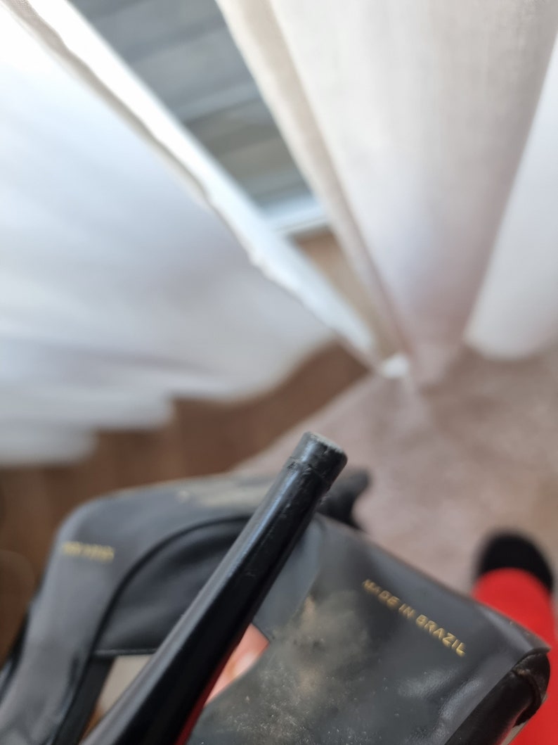 May include: Close-up of a black leather heeled shoe with a gold label that reads "Made in Brazil".