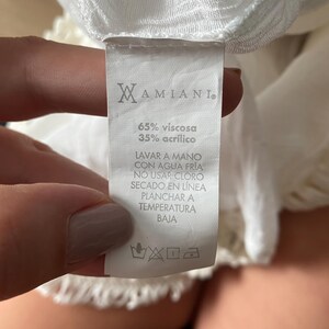 May include: White clothing care label with the brand name "MAMIANI."  The label includes the fabric composition: 65% viscose and 35% acrylic.  The care instructions are written in Spanish: "Lavar a mano con agua fr&iacute;a, no usar cloro, secado en l&iacute;nea, planchar a temperatura baja."