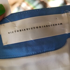 May include: A white label with black text that reads "VICTORIA VICTORIA BECKHAM" and "Made in Portugal". The label is attached to a blue and white striped fabric.
